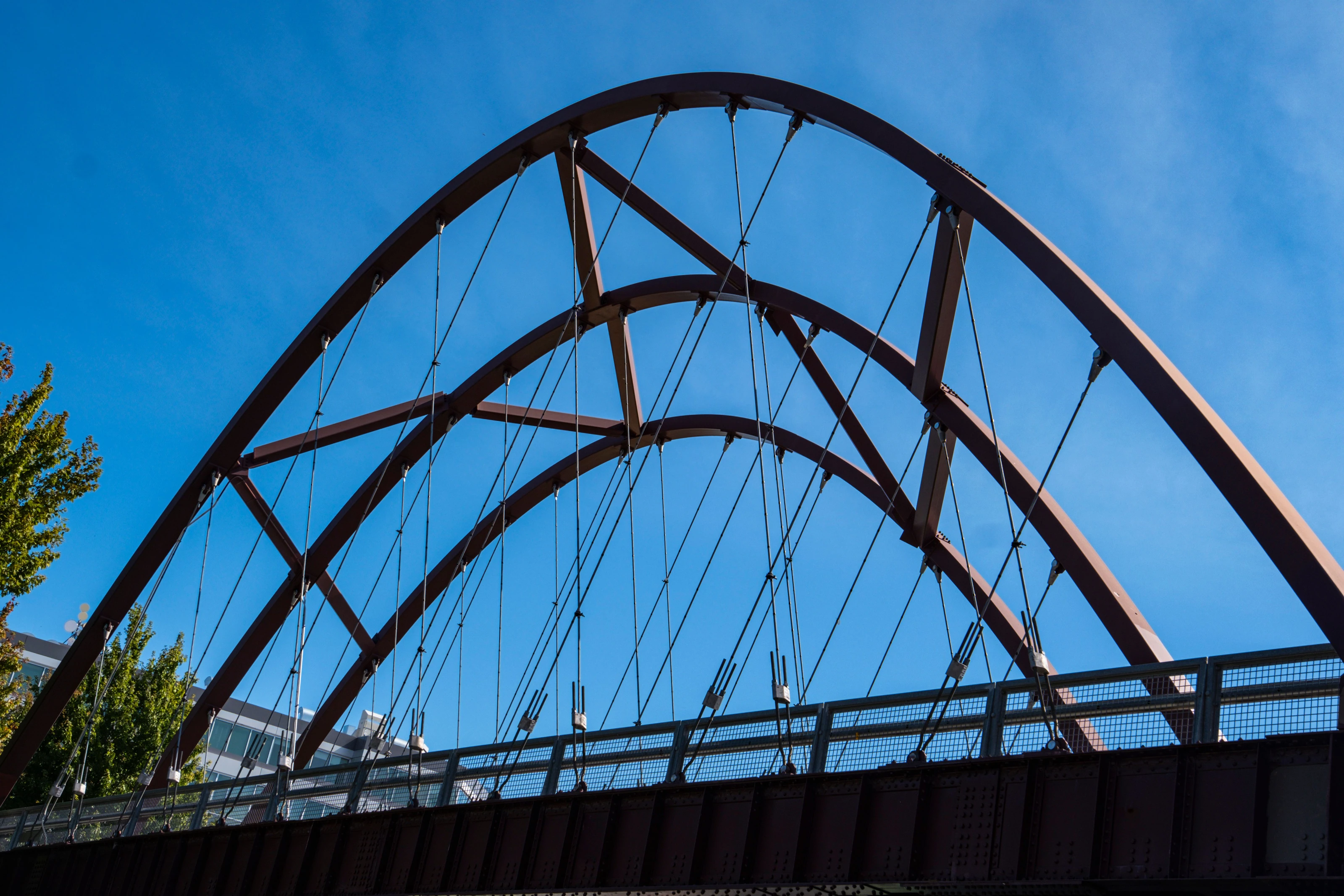 Sweeping steel bridge arches and suspension cables beneath a clear blue daytime sky
