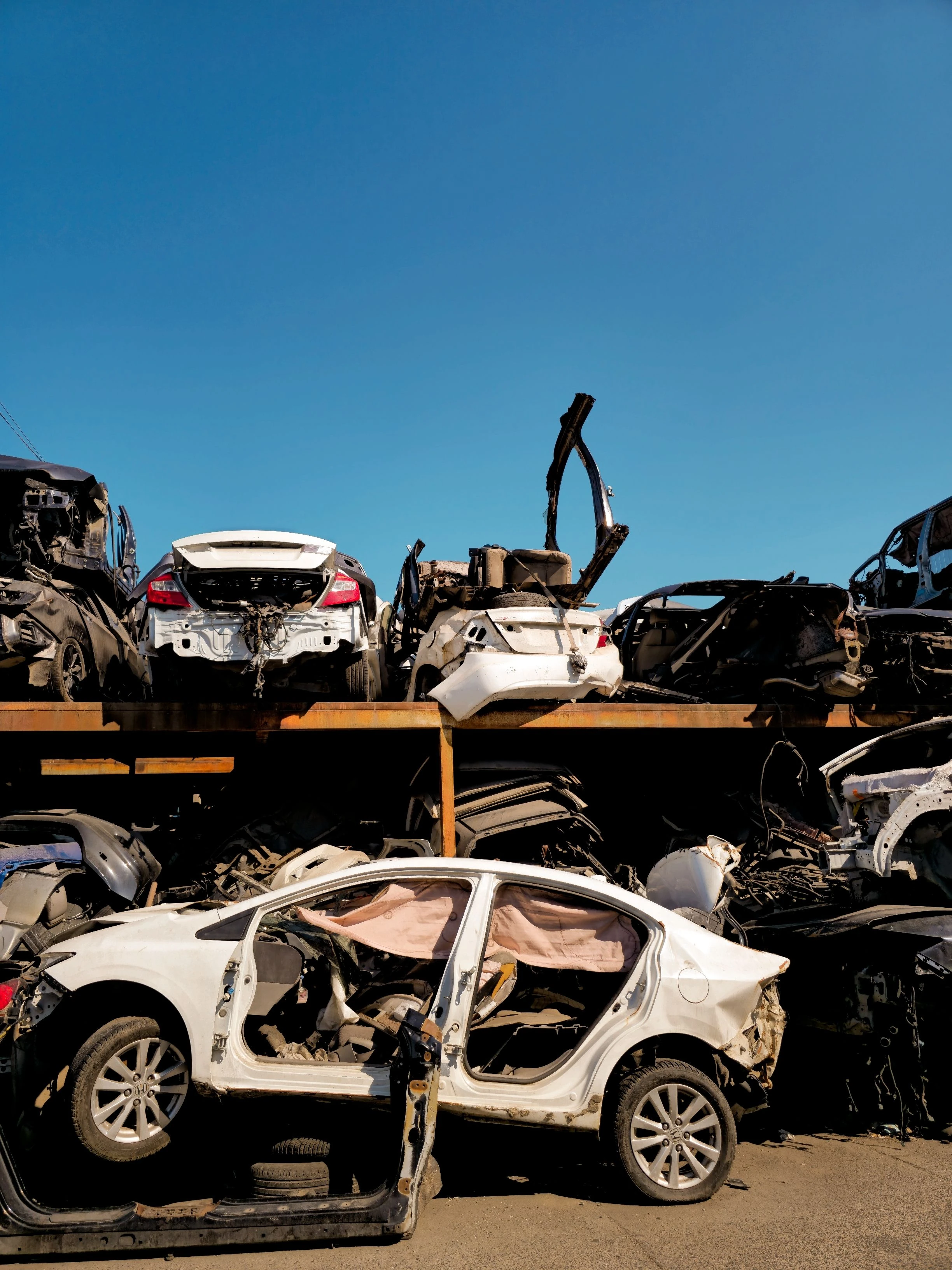 Dismantled cars stacked in a salvage yard beneath a clear blue sky